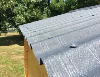 Plaques bitumées gris anthracite fixées par des vis à rondelle posées en sommet d'onde, avec un recouvrement entre deux plaques