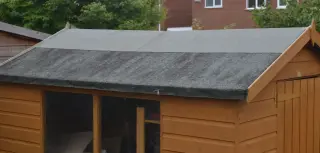 Toit d'abri de jardin couvert de feutre bitumé, la bande basse délavée et marquée de traînées