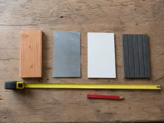 Échantillons de bois douglas, métal galvanisé, PVC et composite alignés sur table en bois avec mètre ruban et crayon de menuisier