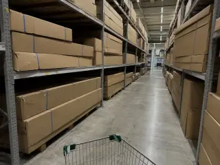 Allée intérieure d'une grande surface de bricolage avec rayonnages métalliques présentant des cartons d'abris de jardin en kit empilés sur trois niveaux