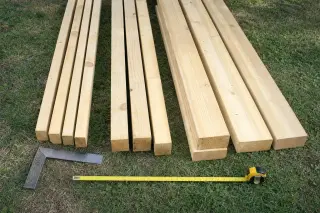 Sections de bois de charpente d'abri de jardin alignées : chevrons, poteaux et sablières en sapin traité, avec mètre ruban et équerre de menuisier