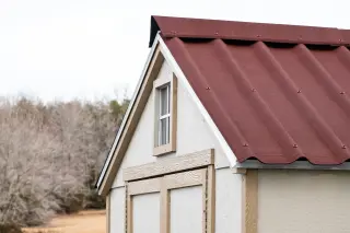 Gros plan sur une toiture d'abri en plaques bitumées ONDULINE EASYFIX® Rouge, fixations à rondelle d'étanchéité intégrée en sommet d'onde et bande de rive blanche le long du pignon