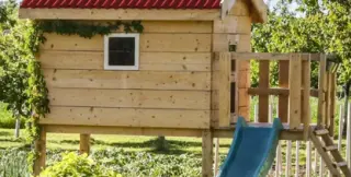 Cabane de jardin en bois clair terminée dans un jardin, toiture en plaques bitumées ondulées ONDULINE® rouge à deux pans, porte et petite fenêtre