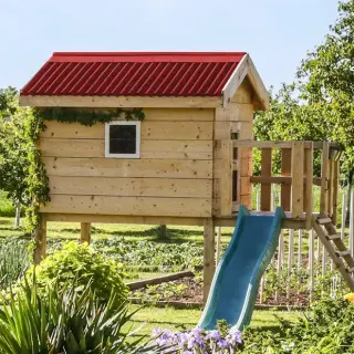 Cabane de jardin en bois clair terminée dans un jardin, toiture en plaques bitumées ondulées ONDULINE® rouge à deux pans, porte et petite fenêtre