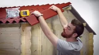 Pose d'une plaque bitumée ondulée ONDULINE EASYLINE sur le toit d'un petit abri, plaques planes bien alignées, fixation en sommet d'onde à la vis à rondelle d'étanchéité intégrée, faîtière et rive en place, débord de 7 cm à l'égout