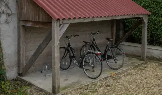 Vélos rangés dans un râtelier au sol boulonné sur la dalle béton d'un abri en bois à toiture ondulée ONDULINE rouge