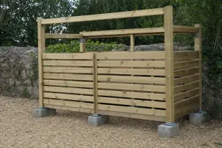 Ossature bois d'un cache-poubelle à claire-voie en cours de montage sur plots, montants et lisses assemblés, lames de bardage espacées pour la ventilation, avant pose de la couverture bitumée